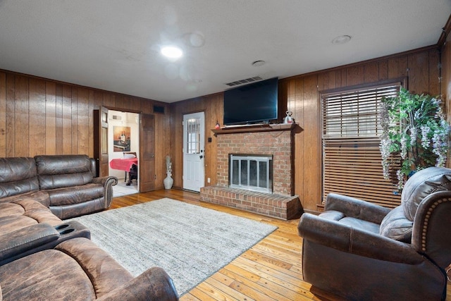 living room with a brick fireplace, light hardwood / wood-style flooring, and wooden walls