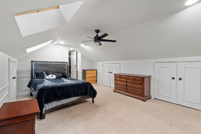 carpeted bedroom featuring multiple closets, ceiling fan, and vaulted ceiling with skylight