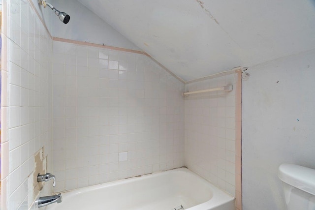 bathroom with vaulted ceiling, toilet, and tiled shower / bath