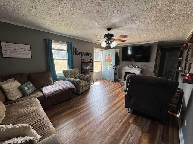 living room with dark wood-type flooring, ceiling fan, ornamental molding, and a textured ceiling