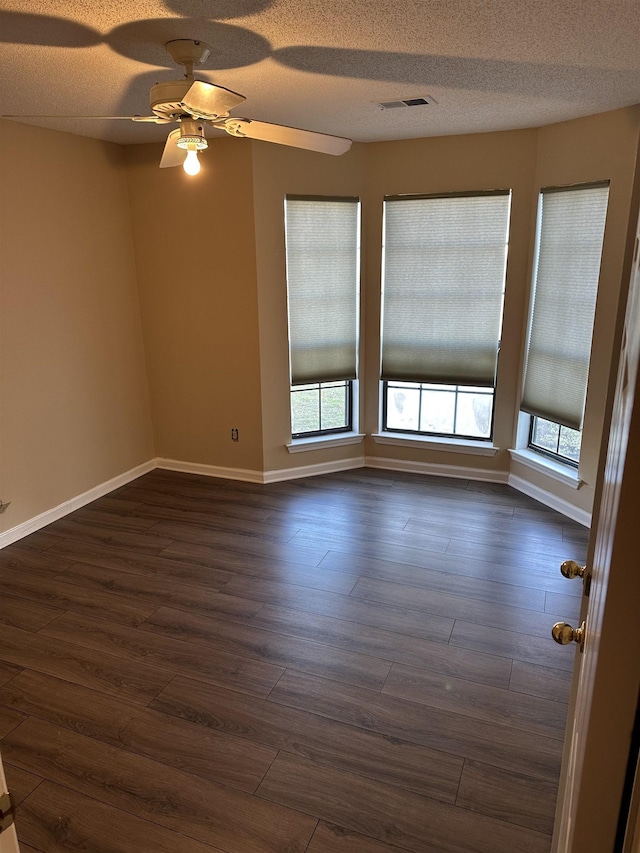 unfurnished room featuring ceiling fan, a wealth of natural light, dark wood-type flooring, and a textured ceiling