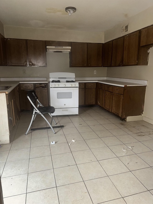 kitchen featuring light tile patterned flooring, dark brown cabinetry, and white gas stove