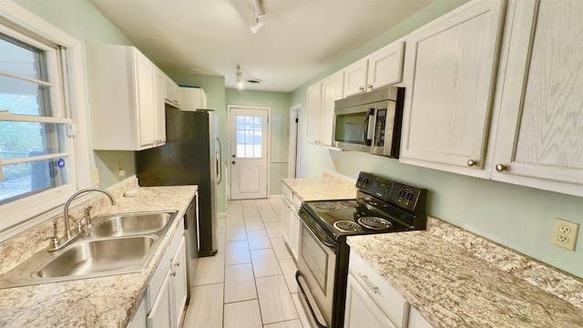 kitchen with appliances with stainless steel finishes, rail lighting, sink, white cabinets, and light stone counters