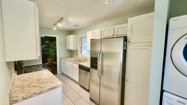 kitchen featuring sink, stainless steel appliances, stacked washer and clothes dryer, light stone countertops, and white cabinets