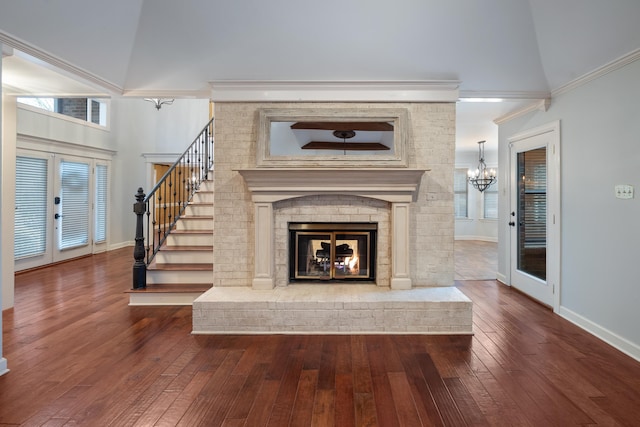 unfurnished living room featuring a towering ceiling, wood-type flooring, a brick fireplace, an inviting chandelier, and french doors