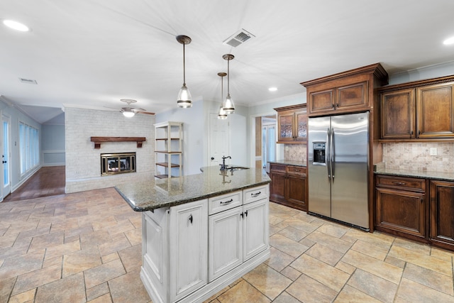 kitchen with stainless steel fridge with ice dispenser, hanging light fixtures, dark stone countertops, a fireplace, and white cabinets