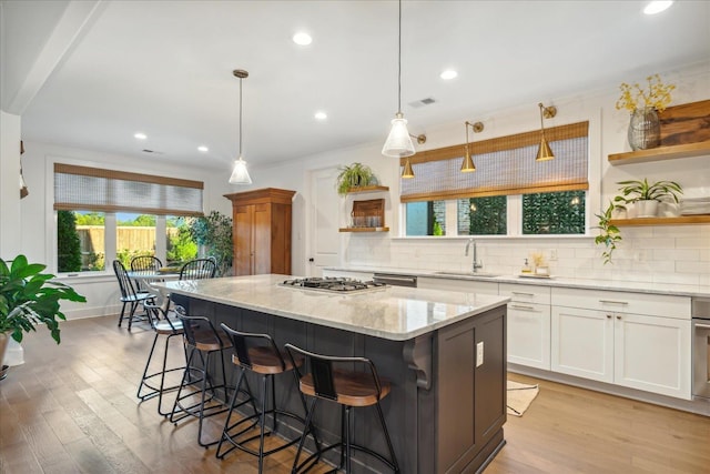 kitchen with sink, a center island, light stone countertops, white cabinets, and decorative light fixtures