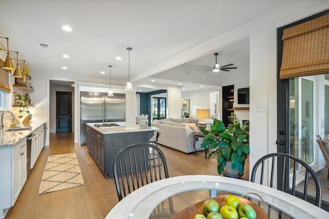 kitchen with light stone counters, light hardwood / wood-style flooring, appliances with stainless steel finishes, pendant lighting, and white cabinets