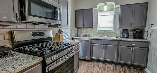 kitchen featuring sink, hardwood / wood-style flooring, stainless steel appliances, light stone countertops, and backsplash