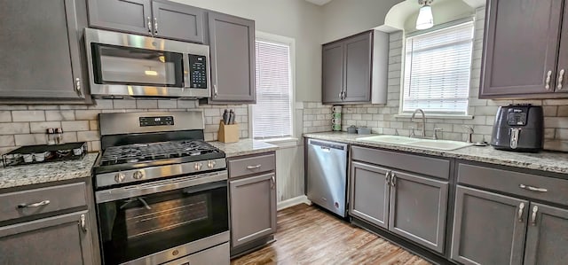 kitchen with sink, gray cabinetry, light stone counters, light hardwood / wood-style flooring, and appliances with stainless steel finishes