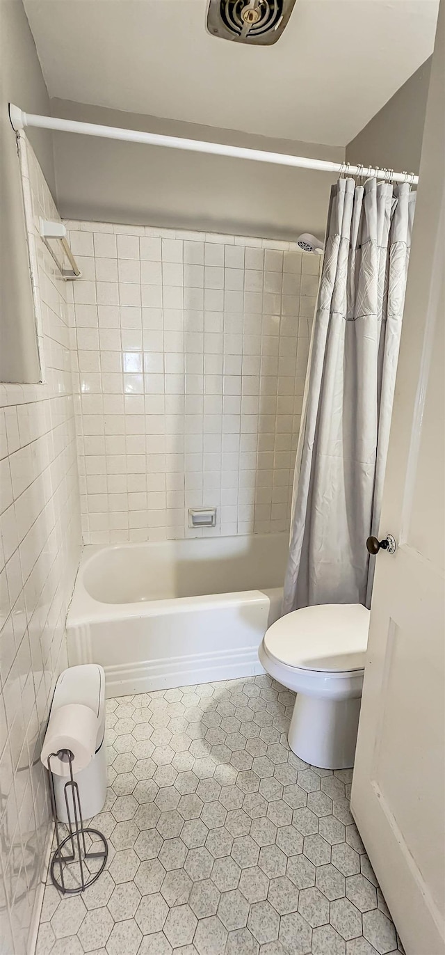 bathroom with tile walls, shower / bath combo, and toilet