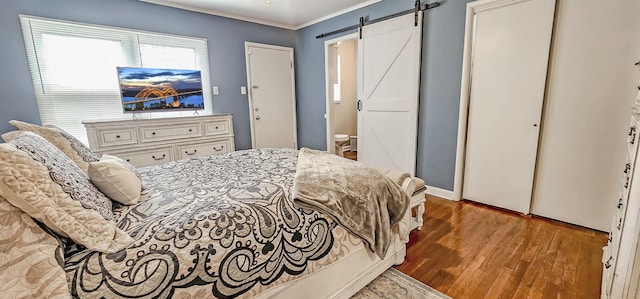 bedroom with crown molding, wood-type flooring, and a barn door