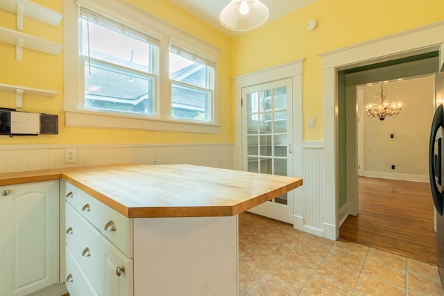 kitchen with butcher block countertops, decorative light fixtures, light tile patterned floors, kitchen peninsula, and white cabinets