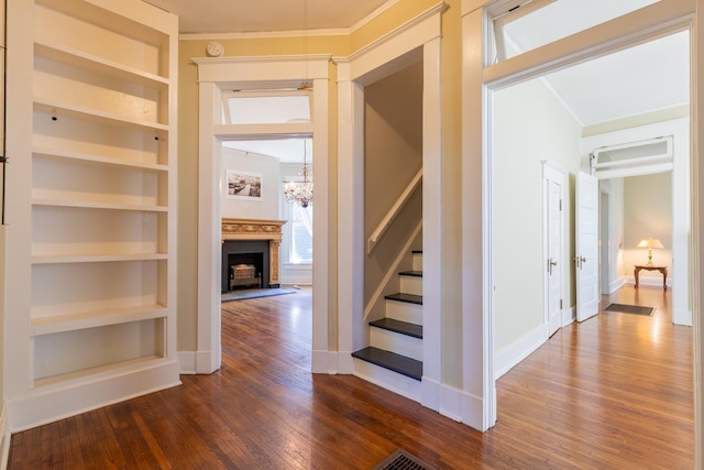 interior space with dark wood-type flooring, ornamental molding, a chandelier, and built in features