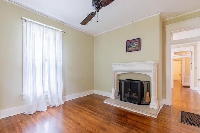 unfurnished living room featuring ceiling fan, ornamental molding, wood-type flooring, and a tile fireplace