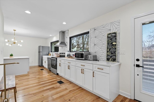 kitchen with wall chimney exhaust hood, white cabinetry, tasteful backsplash, hanging light fixtures, and appliances with stainless steel finishes