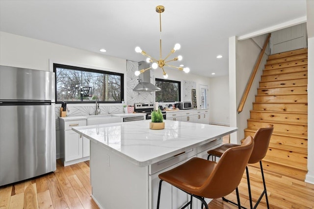 kitchen featuring appliances with stainless steel finishes, white cabinetry, hanging light fixtures, a center island, and exhaust hood