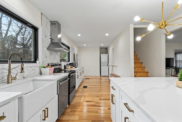 kitchen with backsplash, white cabinets, light hardwood / wood-style floors, stainless steel appliances, and wall chimney range hood