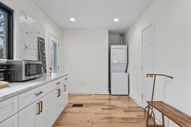 kitchen with stacked washer and dryer, white cabinets, and light hardwood / wood-style flooring