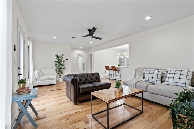 living room with ceiling fan with notable chandelier and light hardwood / wood-style flooring