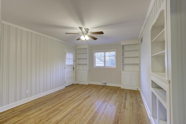 unfurnished room with crown molding, built in shelves, ceiling fan, and light hardwood / wood-style flooring