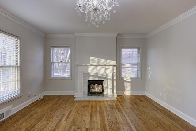 unfurnished living room with an inviting chandelier, hardwood / wood-style flooring, a wealth of natural light, and ornamental molding