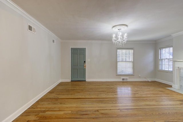 empty room featuring ornamental molding, a notable chandelier, a high end fireplace, and light hardwood / wood-style flooring