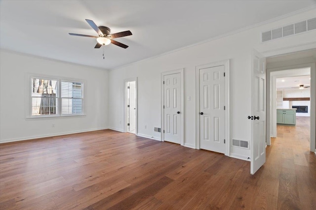 unfurnished bedroom featuring multiple closets, ceiling fan, wood-type flooring, and crown molding