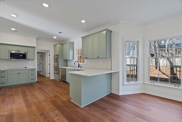 kitchen with hardwood / wood-style floors, stainless steel appliances, a healthy amount of sunlight, green cabinetry, and kitchen peninsula