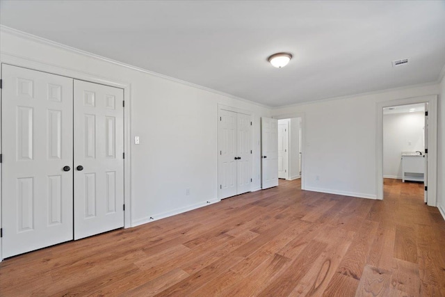 unfurnished bedroom with multiple closets, ornamental molding, and light hardwood / wood-style flooring