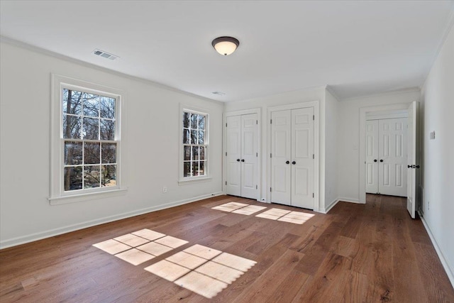 unfurnished bedroom with crown molding, two closets, and dark hardwood / wood-style flooring