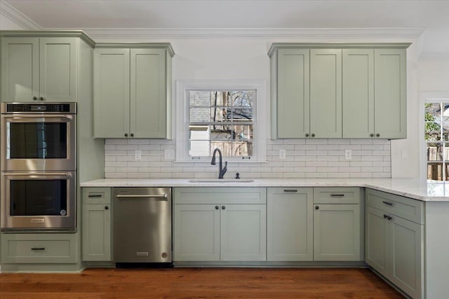 kitchen featuring sink, green cabinetry, ornamental molding, appliances with stainless steel finishes, and light stone countertops