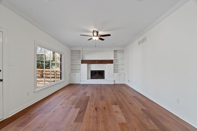 unfurnished living room with ornamental molding, a brick fireplace, light hardwood / wood-style floors, and built in features