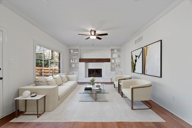 living room featuring built in shelves, ornamental molding, a brick fireplace, and light hardwood / wood-style flooring