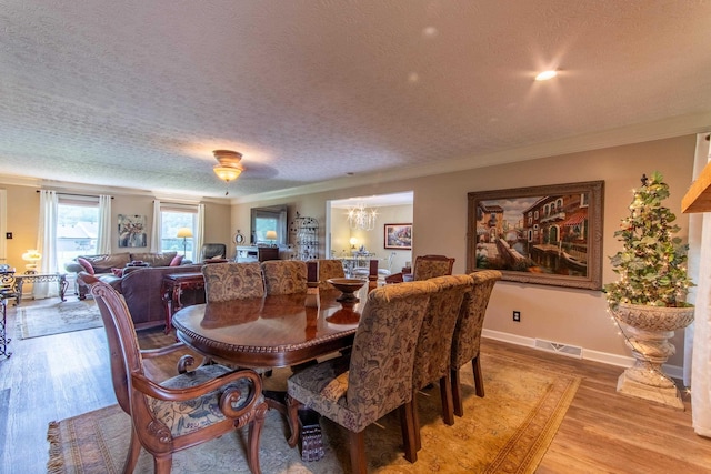 dining area with light hardwood / wood-style flooring, ornamental molding, a chandelier, and a textured ceiling