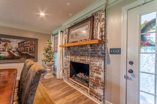 living room with ornamental molding, light hardwood / wood-style floors, a brick fireplace, and a textured ceiling