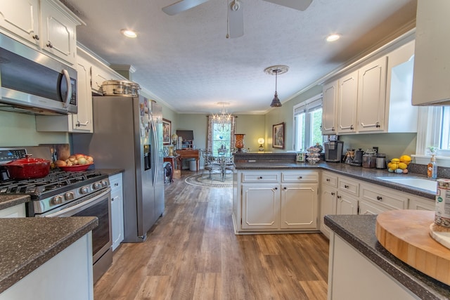 kitchen featuring stainless steel appliances, white cabinetry, ornamental molding, and decorative light fixtures