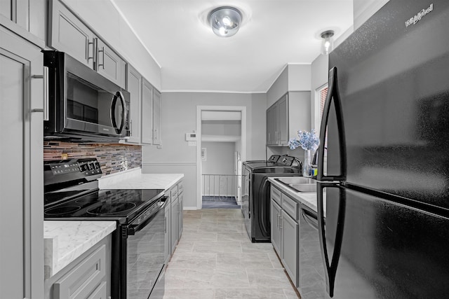 kitchen with gray cabinetry, light stone counters, tasteful backsplash, black appliances, and separate washer and dryer