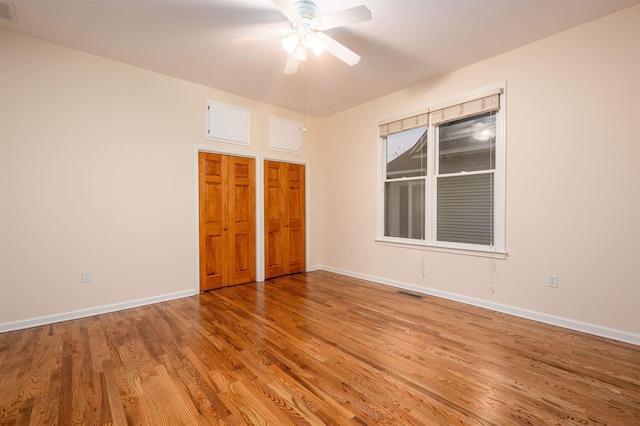 unfurnished bedroom featuring ceiling fan, hardwood / wood-style flooring, and multiple closets