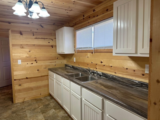 kitchen with pendant lighting, sink, wooden walls, and white cabinets