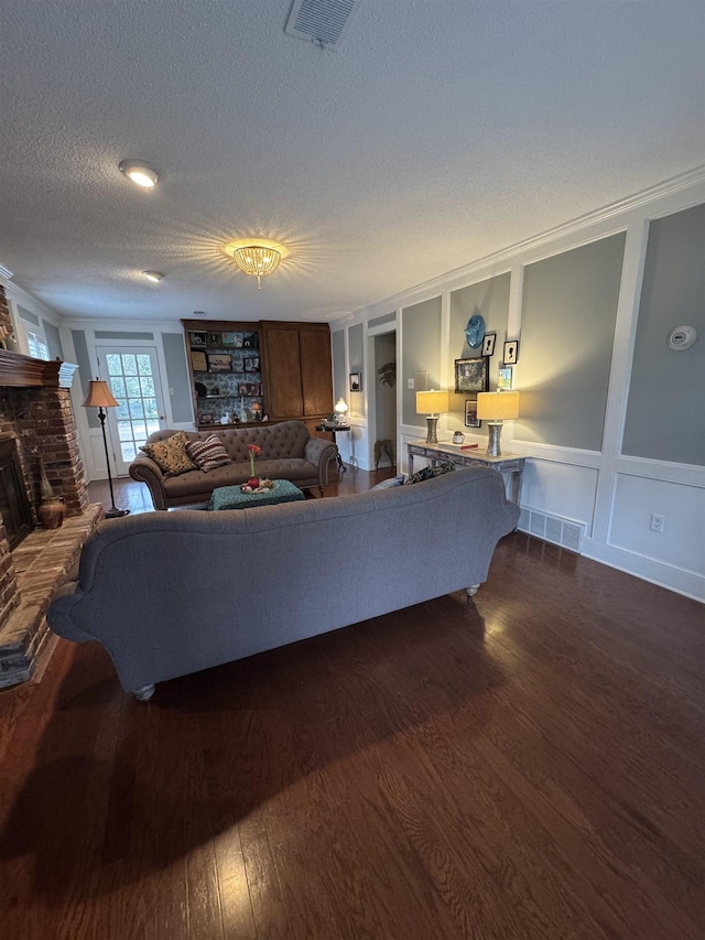 living room featuring dark hardwood / wood-style flooring, a brick fireplace, ornamental molding, and a textured ceiling