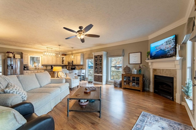 living room featuring a tiled fireplace, crown molding, a textured ceiling, and light wood-type flooring