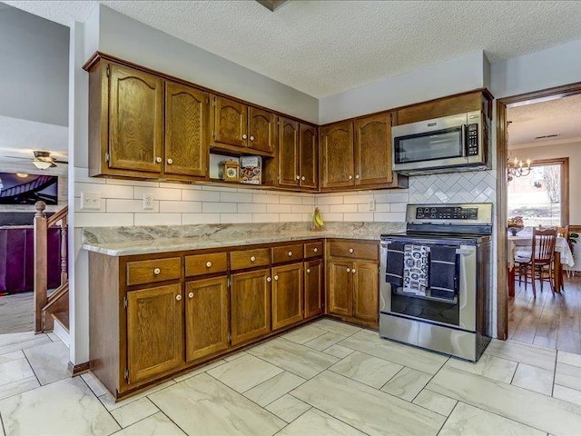 kitchen with tasteful backsplash, an inviting chandelier, a textured ceiling, and appliances with stainless steel finishes