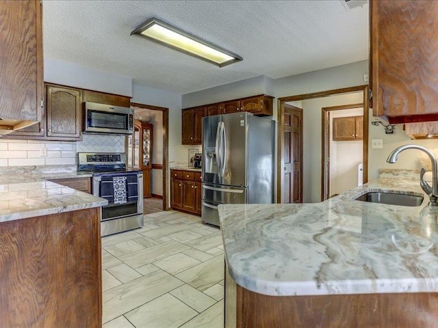 kitchen featuring sink, appliances with stainless steel finishes, tasteful backsplash, a textured ceiling, and kitchen peninsula