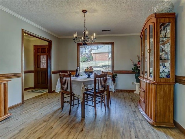 dining area featuring ornamental molding, a chandelier, light hardwood / wood-style flooring, and a textured ceiling