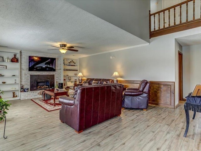 living room featuring wood-type flooring, a textured ceiling, built in features, ceiling fan, and a fireplace