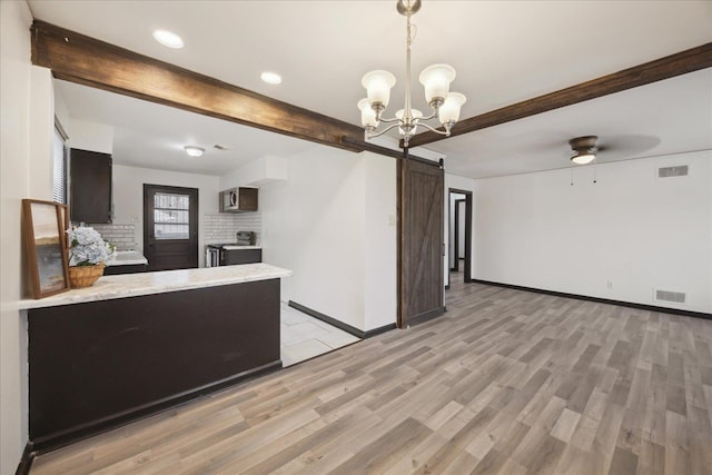 kitchen with appliances with stainless steel finishes, beam ceiling, decorative backsplash, a barn door, and light wood-type flooring