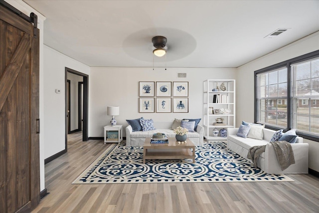 living room featuring ceiling fan, a barn door, and light wood-type flooring