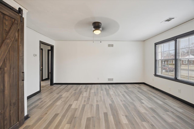 empty room with ceiling fan, a barn door, and light wood-type flooring