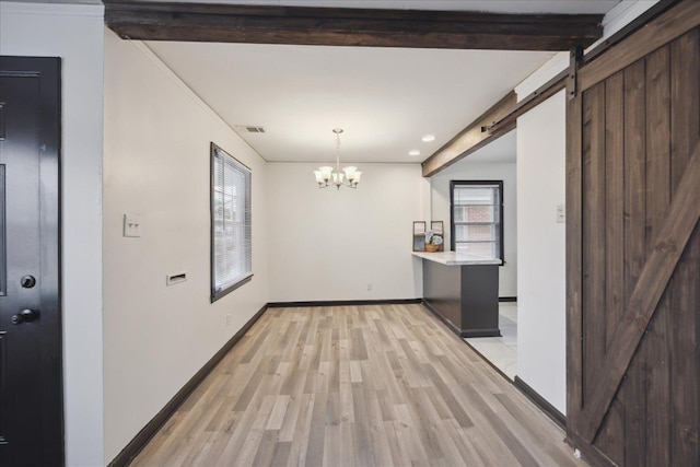 interior space with beam ceiling, a barn door, light hardwood / wood-style floors, and plenty of natural light